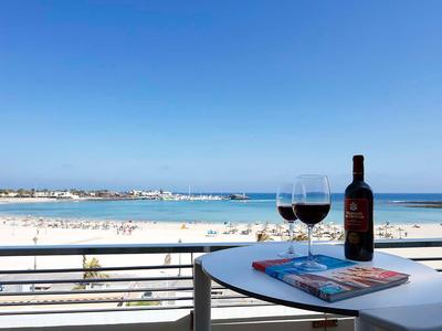 Vista de una playa bajo un cielo despejado con dos copas de vino y una botella en una mesa del balcón.