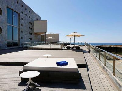 Taras na dachu z leżakami, parasolem i widokiem na morze przy czystym niebie.