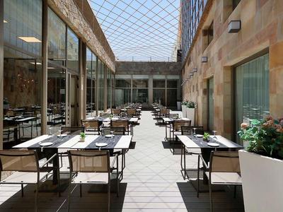 Jasne patio z szklanym dachem, stołami i krzesłami dla gości hotelu lub restauracji.