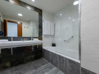 Salle de bain moderne avec grande baignoire, miroir éclairé et carrelage gris.