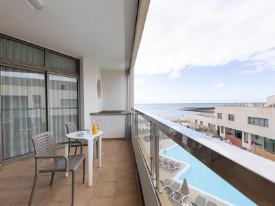 Balcon avec table et chaises, vue sur la piscine et la mer dans un hôtel.