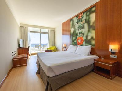 Chambre d'hôtel moderne avec lit double, grande fenêtre et balcon avec vue sur la mer.