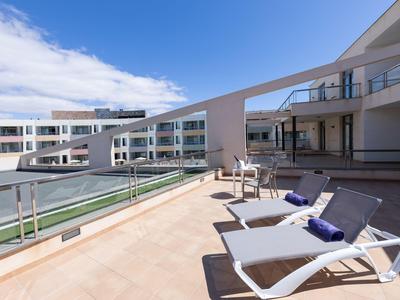 Espace piscine d'hôtel moderne avec chaises longues et rambarde en verre sous un ciel bleu.
