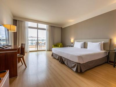 Chambre d'hôtel moderne avec grand lit double, sol en bois, bureau et balcon avec vue sur la mer.