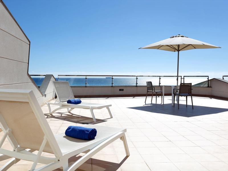 Taras na dachu z leżakami, parasolem i miejscami do siedzenia z widokiem na morze.