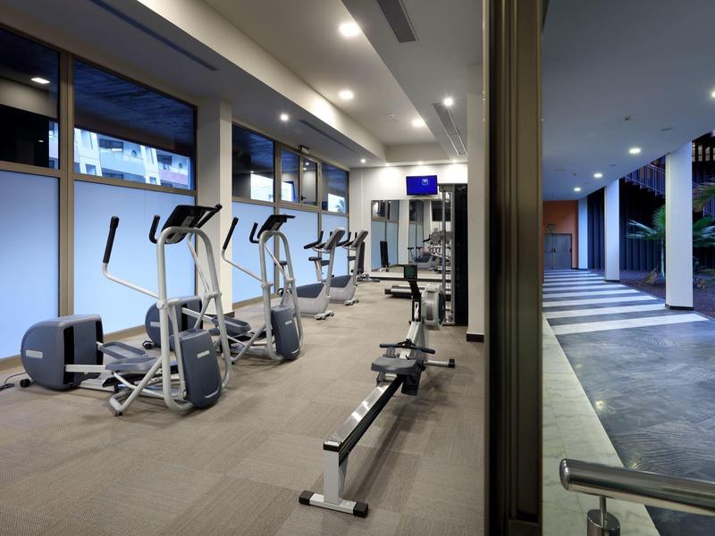 Nowoczesna siłownia z urządzeniami do ćwiczeń i widokiem na teren na zewnątrz.