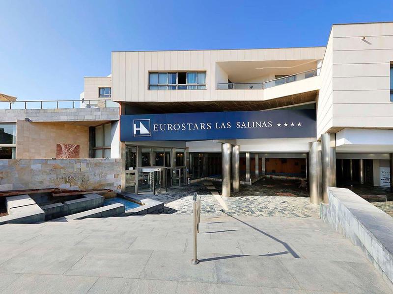 Nowoczesne wejście do hotelu z szerokim wejściem i dużymi balkonami na wyższym piętrze.