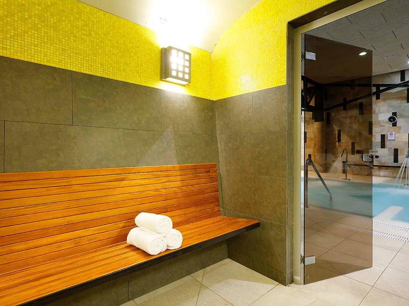 Nowoczesny pokój relaksacyjny z drewnianą ławką, ręcznikami i widokiem na basen.