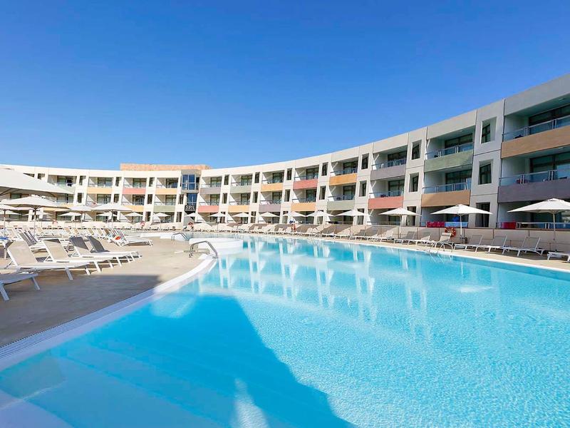 Nowoczesny basen hotelowy z leżakami pod jasnym niebieskim niebem.