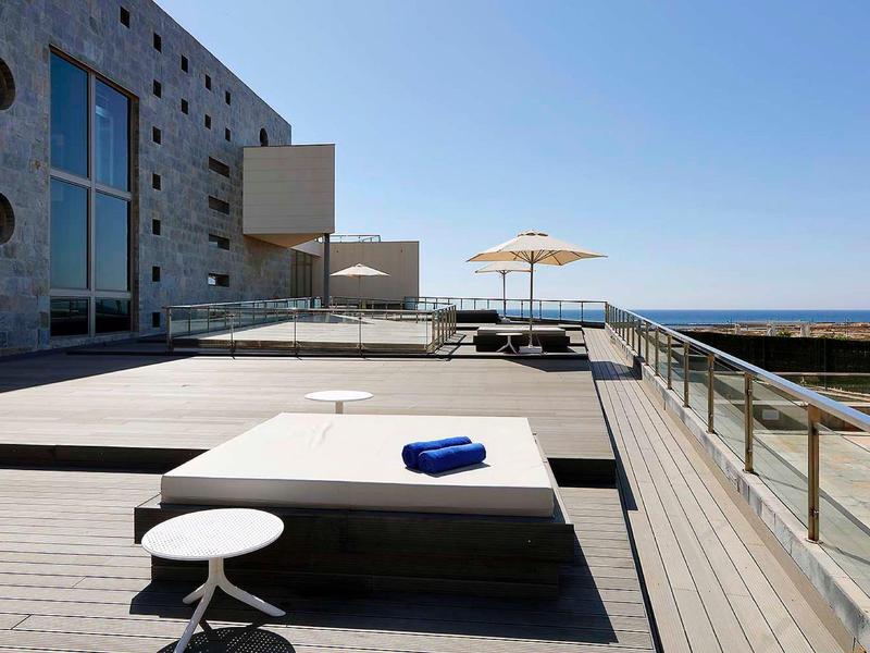 Taras na dachu z leżakami, parasolem i widokiem na morze przy czystym niebie.