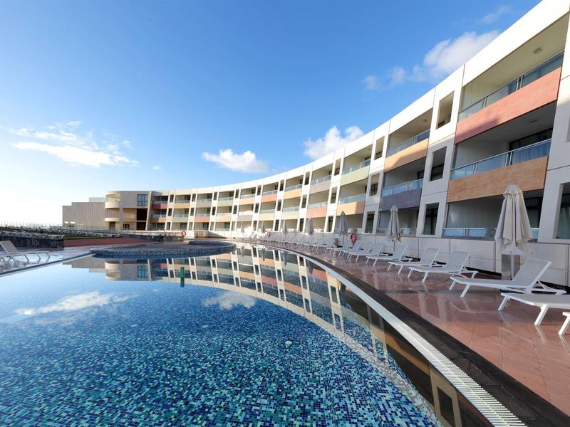 Nowoczesny kompleks hotelowy z wydłużonym basenem i białymi leżakami.