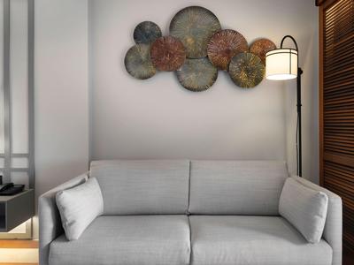 Modern eingerichtetes Zimmer mit grauem Sofa, Wandkunst und Stehlampe neben Holzjalousien.