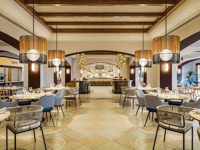 Helles, modernes Hotelrestaurant mit Holzdecken, runden Tischen und stilvollen Lampen.