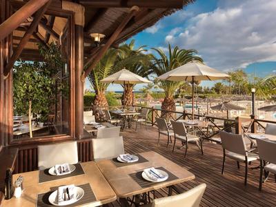 Gemütliche Terrasse eines Hotels mit eingedeckten Tischen, Stühlen und Sonnenschirmen unter blauem Himmel.