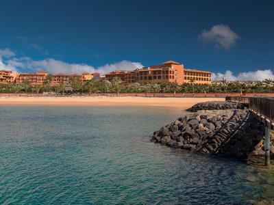 Hotelanlage am Strand mit klarem Wasser und Steg unter blauem Himmel.