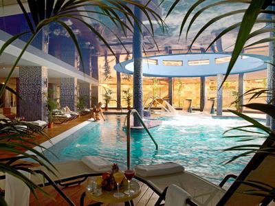 Innenpool in einem Hotel mit Wasserfällen, Liegestühlen und tropischer Dekoration.