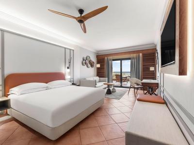Modernes Hotelzimmer mit großem Bett, Deckenventilator und Balkon mit Meerblick.