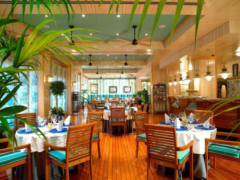 Elegant restaurant met houten meubels, witte tafelkleden en blauwe servetten in een lichte ruimte.