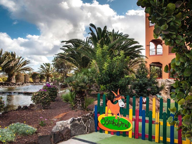 Kleurrijke poort naar een tropische tuin met palmbomen en bloeiende planten naast een vijver.
