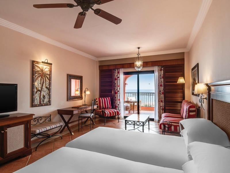 Modern ingerichte hotelkamer met twee bedden, bureau en balkon met uitzicht op zee.