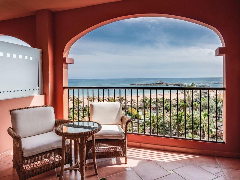 Balkon met twee stoelen en een tafel met uitzicht op zee en strand.