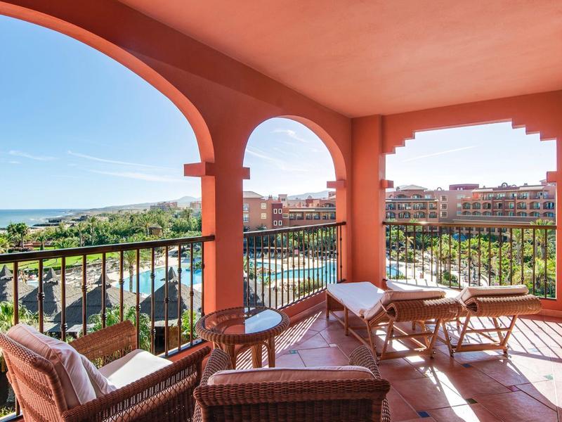 Balkon met zitmeubels en uitzicht op zwembad en zee in een hotelresort.