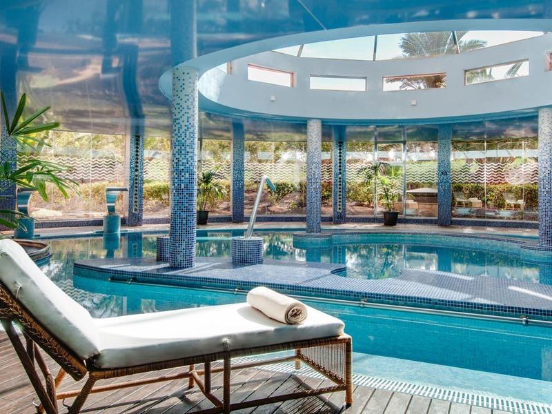 Elegante binnenzwembad met een ligstoel en grote ramen met uitzicht op buiten.