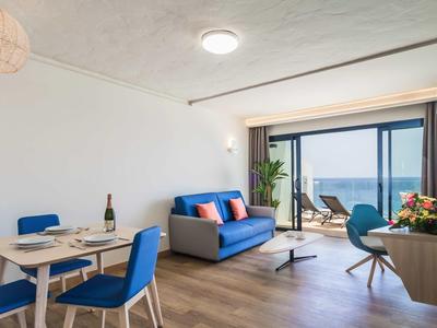 Moderner Wohnraum mit blauem Sofa, blauem Essbereich, Holzfußboden und großem Fenster mit Meerblick.