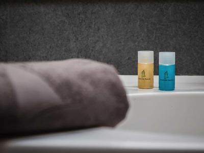 Biała umywalka z dwoma małymi butelkami szamponu i żelu pod prysznic oraz szary ręcznik.