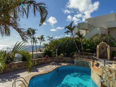 Una piccola piscina ocra con acqua blu davanti a un edificio bianco sotto un cielo azzurro.