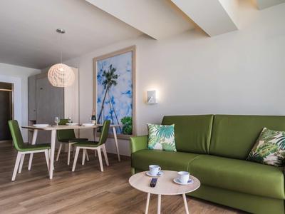 Helles Wohnzimmer mit grünem Sofa, Holzfußboden, kleinem Tisch und Essbereich mit Stühlen.