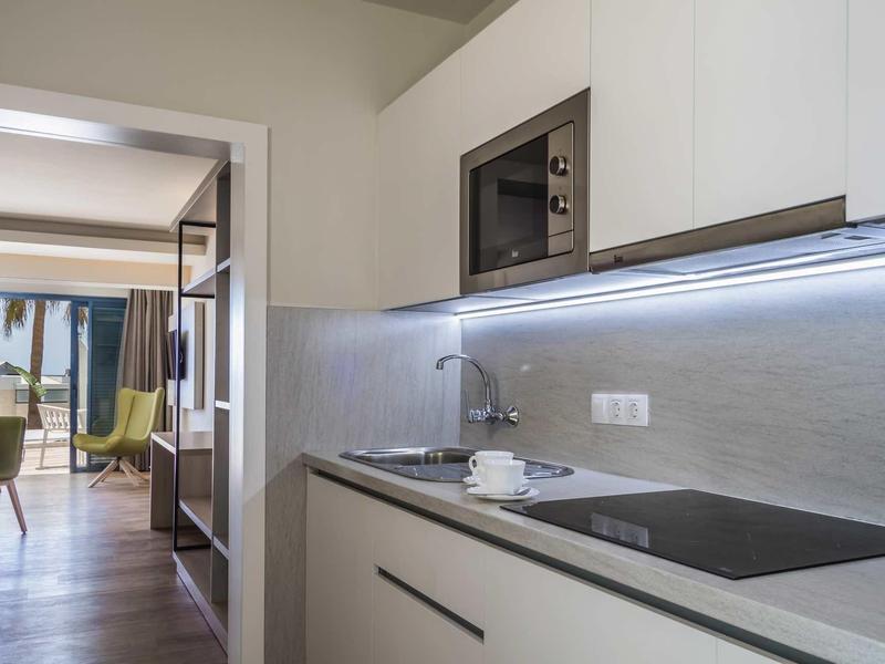 Moderne Küche mit weißen Schränken, Kochfeld, Mikrowelle und Blick ins helle Wohnzimmer.