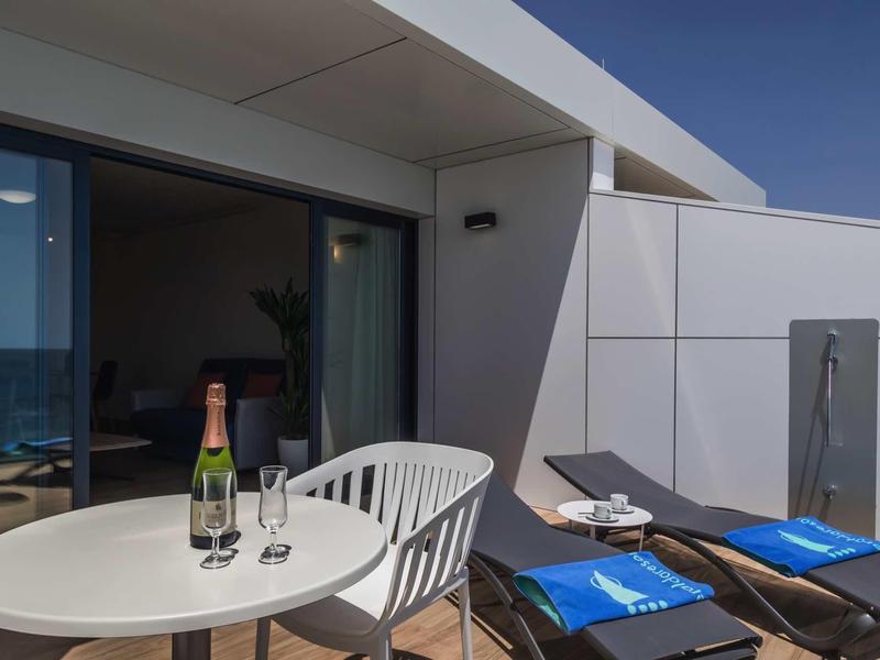 Moderner Balkon mit weißem Tisch, zwei Stühlen, Champagnerflasche, Gläsern und blauen Handtüchern.