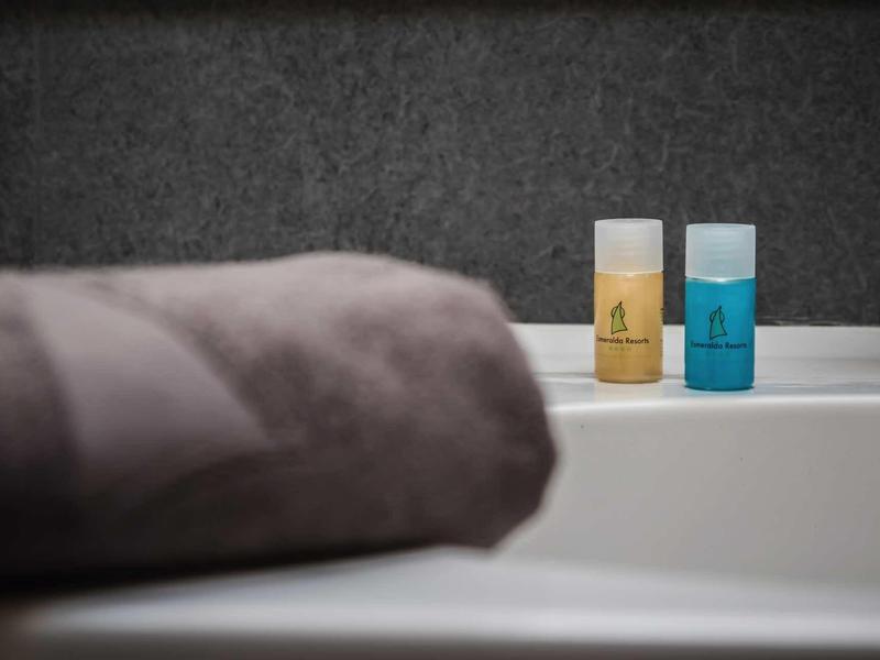 Zwei kleine Flaschen Shampoo stehen auf einem weißen Waschbeckensims, davor liegt ein graues Handtuch.