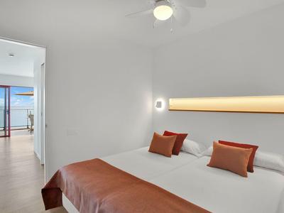 Jasno urządzona sypialnia z dużym łóżkiem i dostępem do balkonu z widokiem na morze.