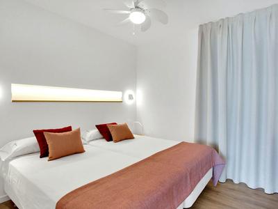 Nowoczesny pokój hotelowy z podwójnym łóżkiem, białymi ścianami i miękkimi zasłonami.