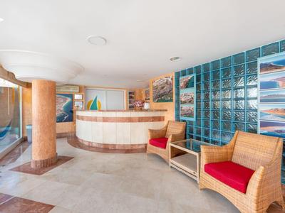 Jasna lobby hotelowa z recepcją, czerwonymi fotelami i niebieskimi szybami szklanymi.