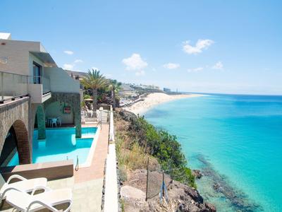 View from a hotel balcony over a pool and a long coast with turquoise sea.