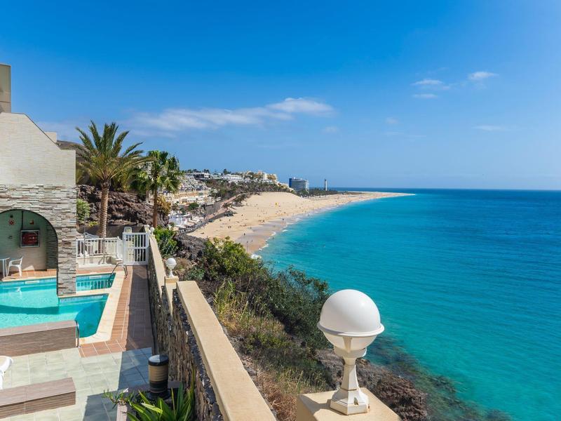 Widok na plażę z turkusowym morzem obok tarasu z basenem.