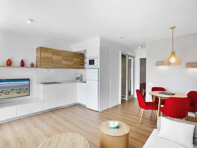 Jasny, nowoczesny salon z otwartą kuchnią, czerwoną jadalnią i drewnianą podłogą.