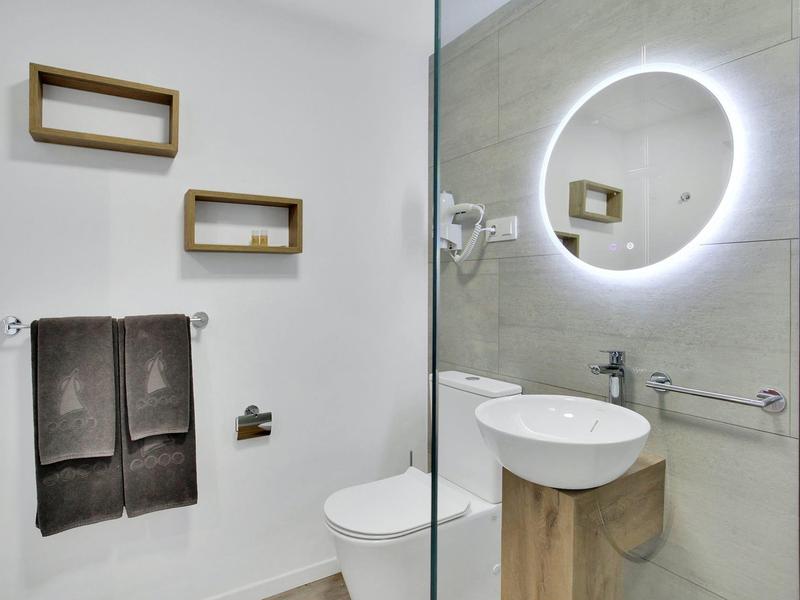 Nowoczesna łazienka z podświetlanym lustrem, umywalką i ręcznikami na białych i szarych ścianach.