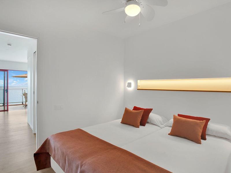 Jasno urządzona sypialnia z dużym łóżkiem i dostępem do balkonu z widokiem na morze.