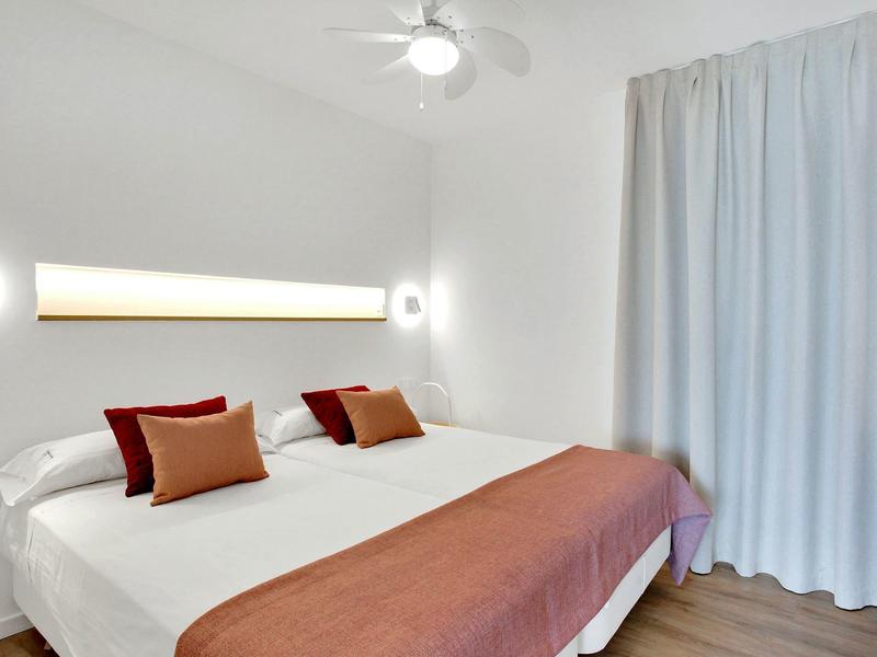 Nowoczesny pokój hotelowy z podwójnym łóżkiem, białymi ścianami i miękkimi zasłonami.