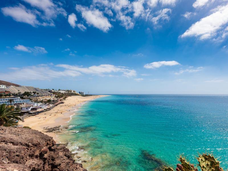Czyste niebieskie morze i piaszczysta plaża z domami pod niebieskim niebem z chmurami.