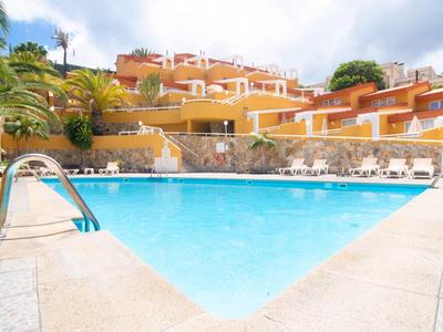Großer Außenpool vor einem terrassenförmigen Gebäude mit Sonnenschirmen und Palmen.