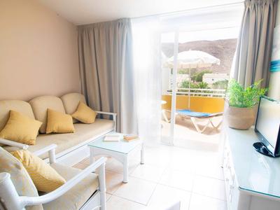 Helder ingericht woonkamer met bank, fauteuils en toegang tot een balkon met parasol.