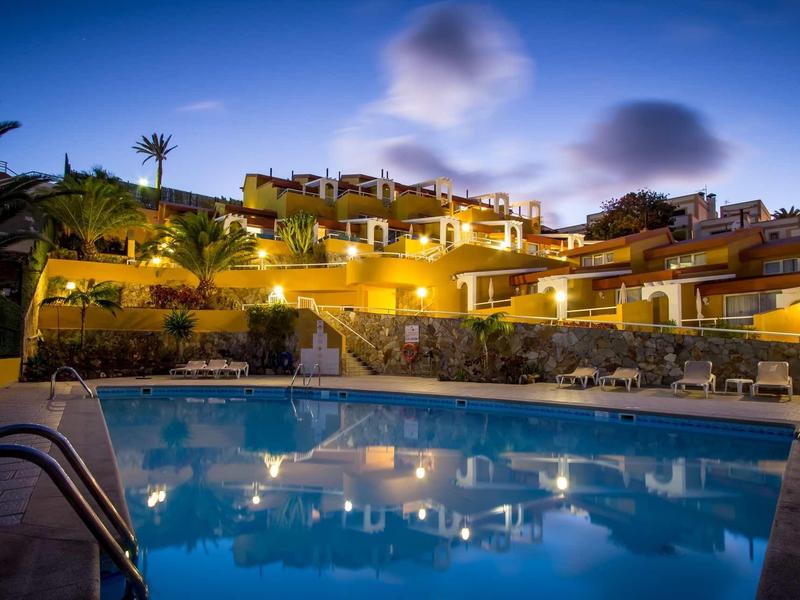 Verlicht hotel met zwembad en palmbomen bij schemering