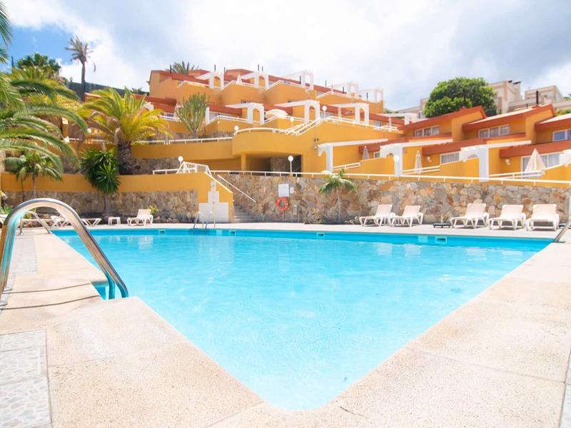 Helder zwembad voor een terrasvormig hotel met palmbomen en zonneschijn.