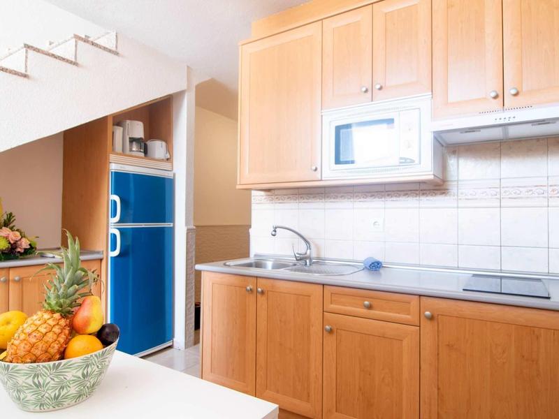 Moderne kleine keuken met houten kasten, magnetron en fruitmand op tafel.