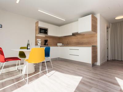 Moderne Küche mit weißen Schränken, Holzrückwand und bunten Stühlen am kleinen Esstisch.